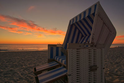 Hooded beach chair on shore against sky during sunset