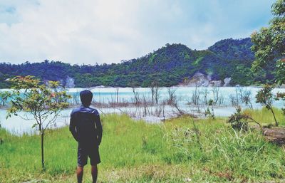 Rear view of man standing by lake against sky