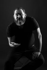 Portrait of young man sitting against black background