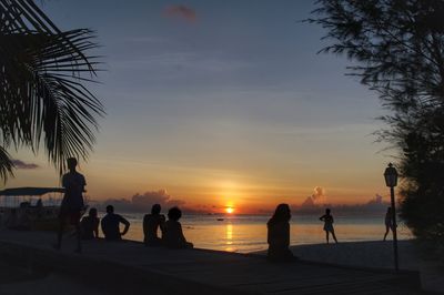 Silhouette people on beach against sky during sunset