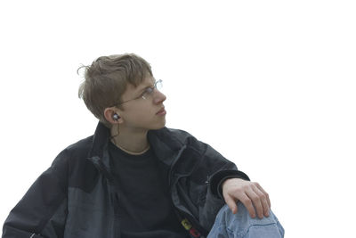 Teenage boy listening music while sitting against clear sky