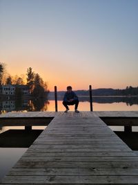 Rear view of man on pier over lake against sky during sunset