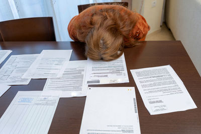 High angle view of depressed woman keeping head on table with document