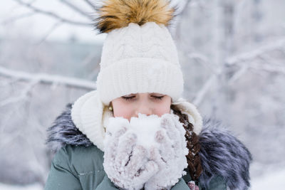 A girl in warm clothes holds snow in her hands in gloves in a winter park. winter lifestyle portrait