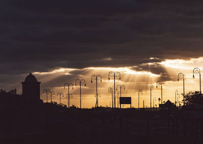 Silhouette street and buildings against sky at sunset