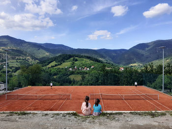 Rear view of girls sitting at court against sky