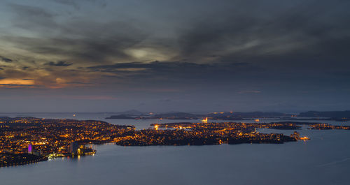 Aerial view of illuminated cityscape by sea against sky during sunset