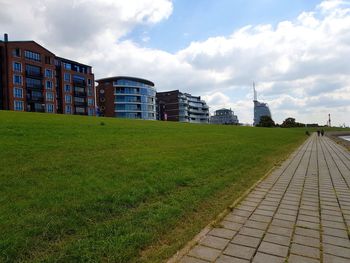 Footpath by buildings in city against sky