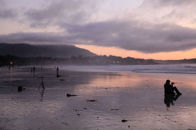 Silhouette people on beach against sky during sunset