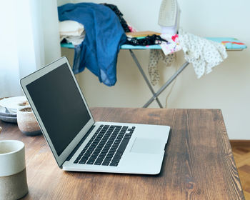 View of laptop with messy clothes on table at home