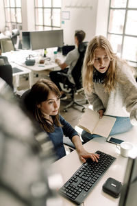 Female professionals discussing while working on computer at workplace