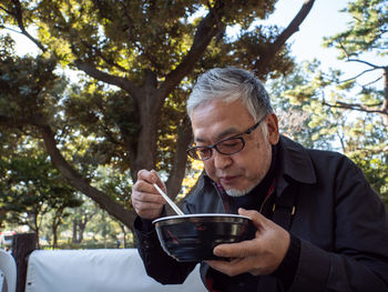 An older asian man eating noodles and soup with chopsticks