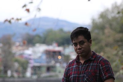 Portrait of young man wearing eyeglasses while standing against landscape