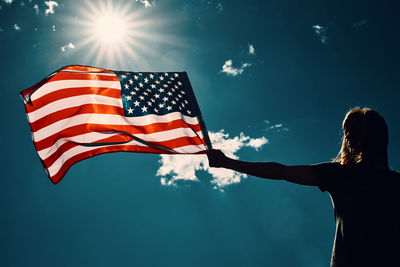 American flag outdoors. woman silhouette holds usa national flag against blue cloudy sky.