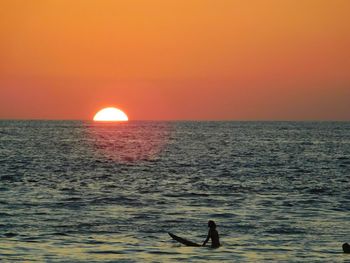 Silhouette person on sea against orange sky during sunset