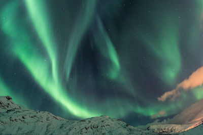 Scenic view of aurora polaris above snowcapped mountains against sky at night