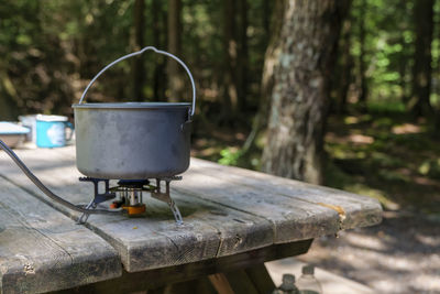 A titanium pot for making food on a gas stove on a camping wooden table in the forest.