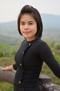 Portrait of young woman standing by railing on observation point against sky