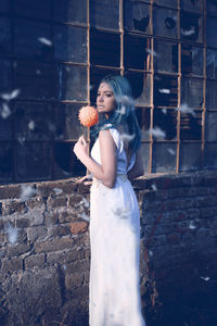 Beautiful woman with flower standing against wall