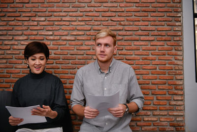 Candidates with resume sitting against brick wall in office