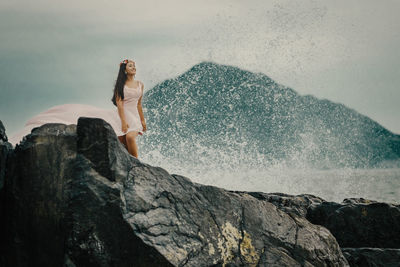 Woman standing on rock by sea against sky