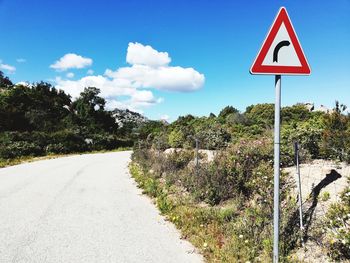 Road sign by trees against sky in city