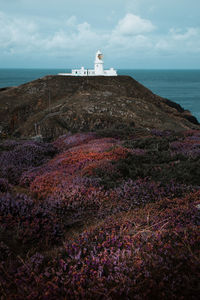 Lighthouse on cliff by sea against sky