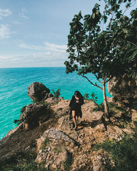 Full length of woman standing on rock against sea