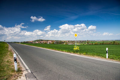 Road sign on field against sky