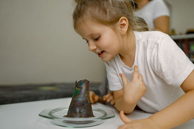 Child girl at home, looking into the mouth of plasticine volcano, curiosity