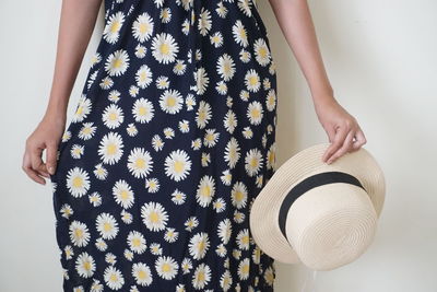 Midsection of woman holding hat against wall