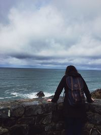 Rear view of woman standing by railing while looking at sea against sky