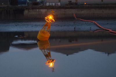 Reflection of man on illuminated fire in lake at dusk