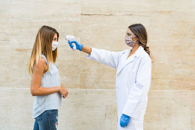 Side view of doctor examining woman while standing by wall outdoors