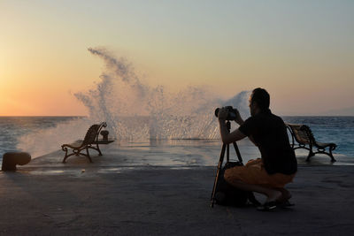 Men sitting on beach against sky during sunset