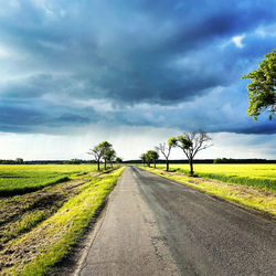 Empty road amidst field against sky