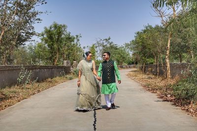 Full length portrait of friends walking on road amidst trees