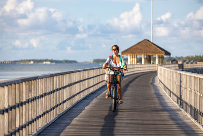 Middle aged woman riding a bicycle on a pathway near the ocean