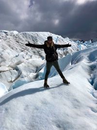 Portrait of woman with arms outstretched standing against snowcapped mountains 