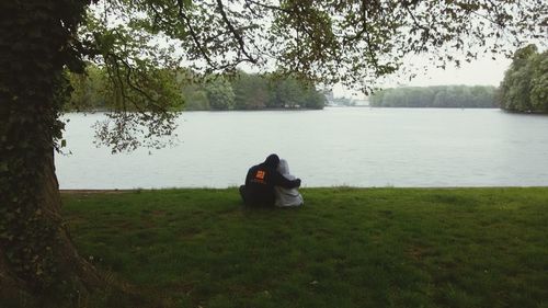 Woman sitting on grass by lake against sky