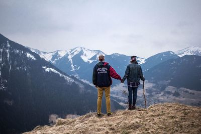 Rear view of men standing on mountain against sky