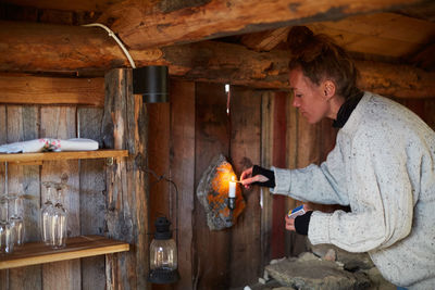 Side view of mid adult woman lighting candle in cottage