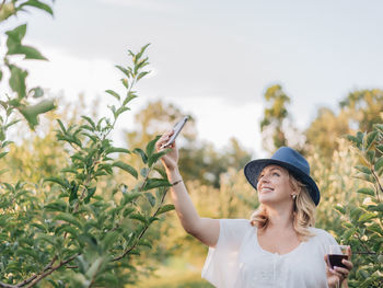 Young millennial woman outdoors at apple orchard taking selfie with smart phone