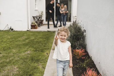 Portrait of girl showing magic wand with family in background at yard