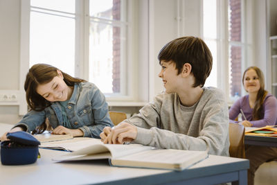 Happy boy laughing while female friend sitting at desk in classroom