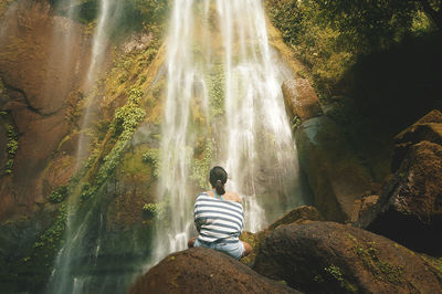 Rear view of woman sitting at waterfall