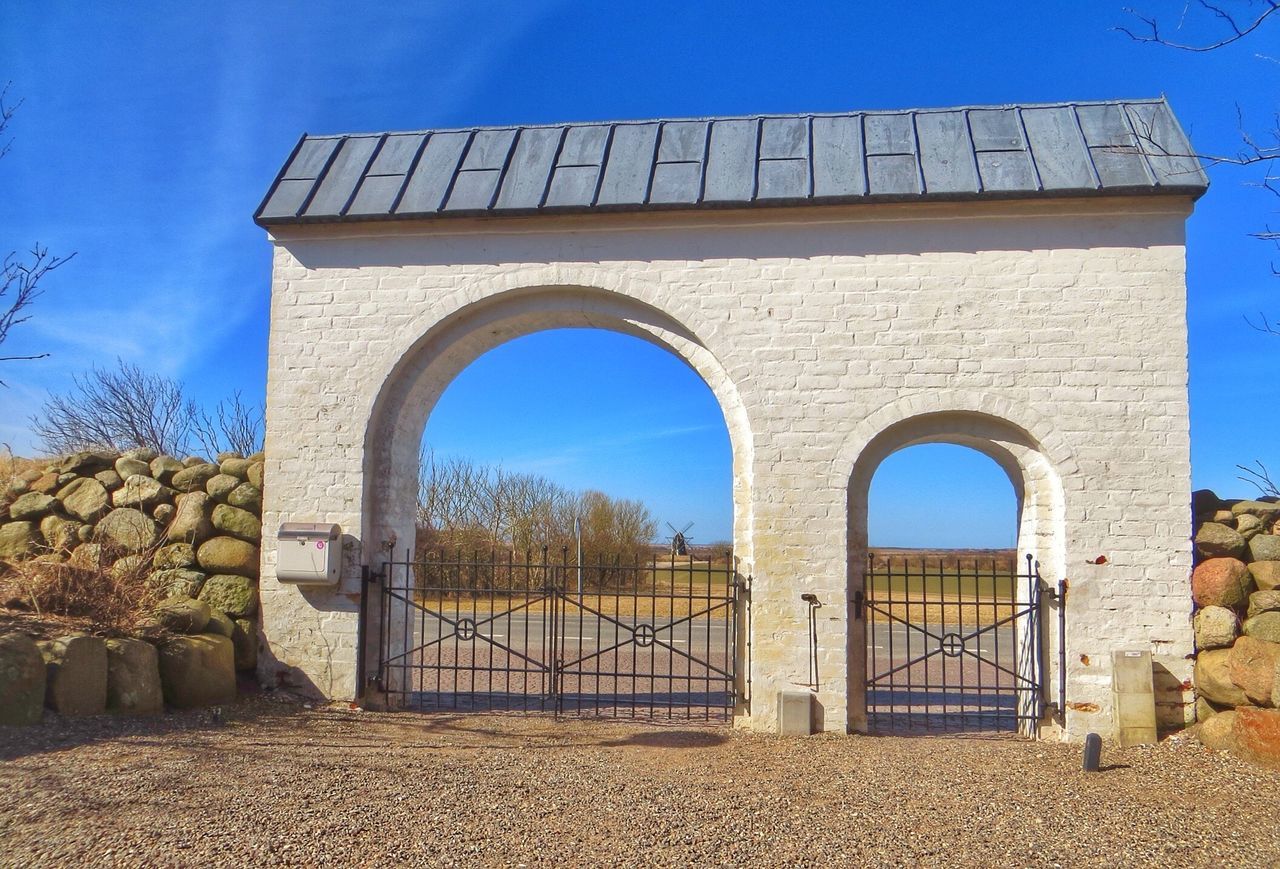 architecture, built structure, building exterior, arch, blue, sky, stone wall, window, house, wall - building feature, day, low angle view, sunlight, gate, wall, brick wall, no people, railing, outdoors, tree