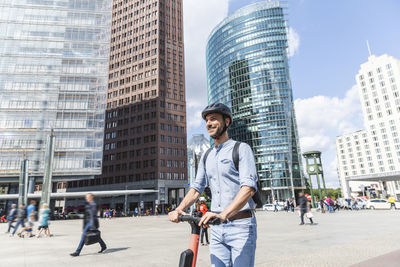 Businessman with e-scooter on city square, berlin, germany