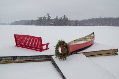 Red bench and red canoe on a snow covered dock 