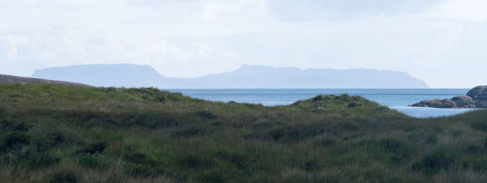 Scenic view of field by sea against sky